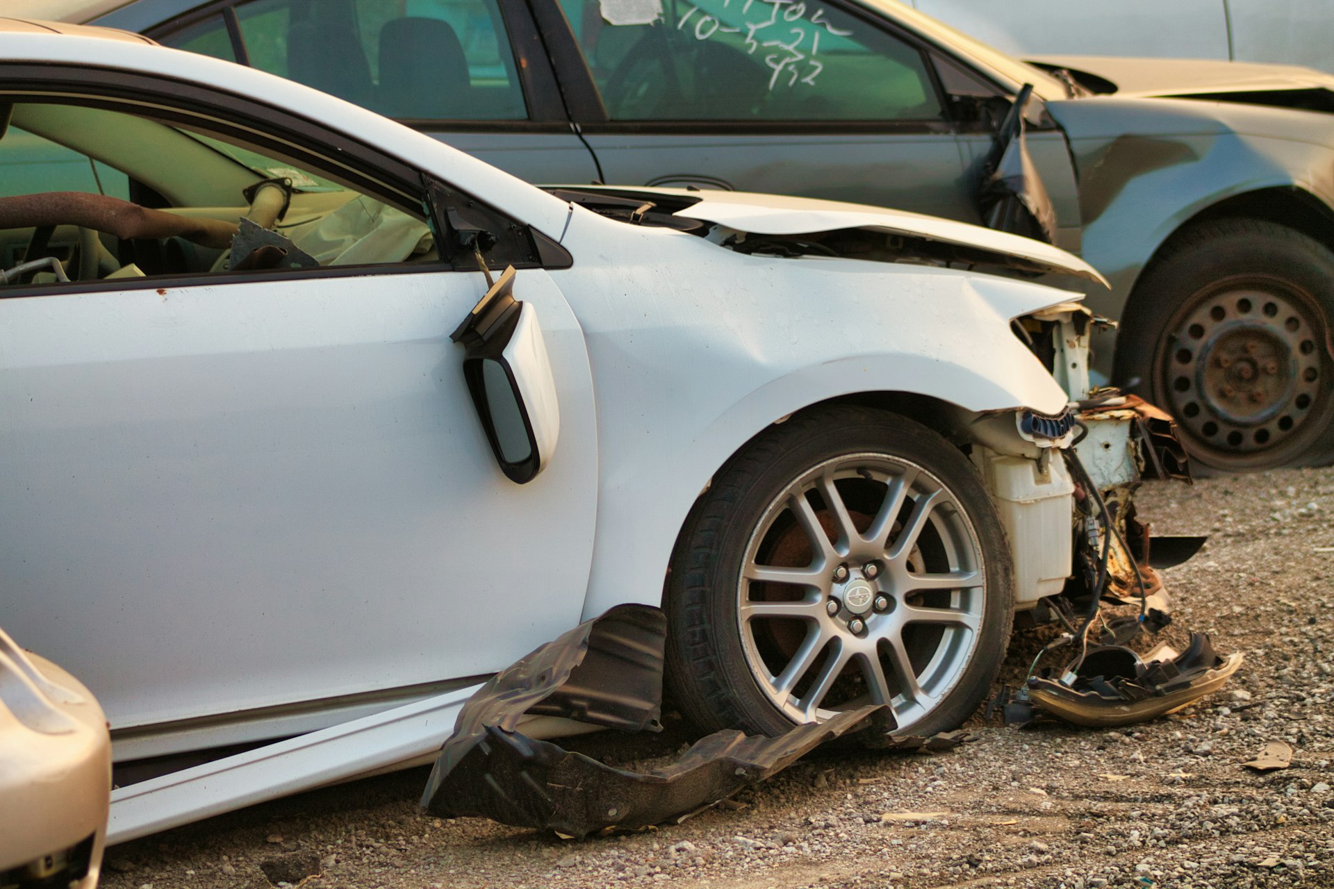 Weißes Unfallfahrzeug mit zerstörter Front auf einem Verwertungsplatz